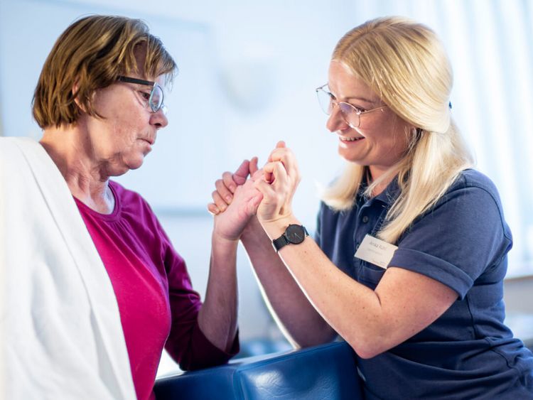 Therapeutin behandelt Hand einer älten Patientin in der Ergotherapie